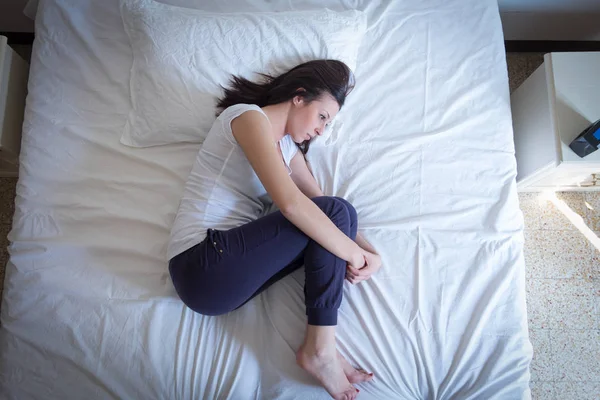 Triste kvinde liggende i sengen i fosterstilling - Stock-foto