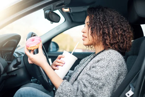 Женщина ест сладкое и пьет за рулем машины — стоковое фото