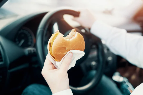 Hombre comiendo una hamburguesa y conduciendo sentado en coche — Foto de Stock