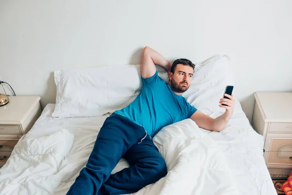 Retrato de hombre en cama blanca usando smartphone —  Fotos de Stock