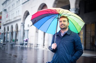 Rainy day in the city and businessman holding umbrella clipart
