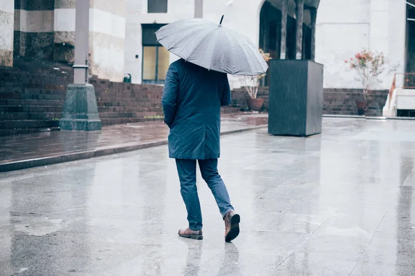 Человек, гуляющий по городу с зонтиком в дождливый день — стоковое фото