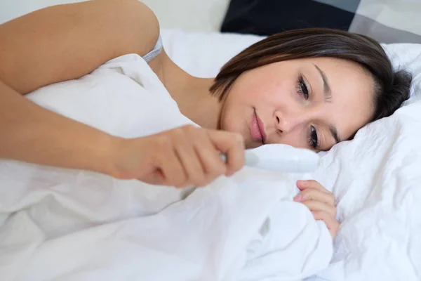 Sick girl lying in on the bed and watching the thermometer — Stock Photo, Image