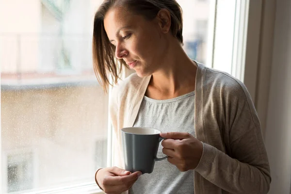 Sad pensive woman holding a cup of coffee portrait next to a win — Stock Photo, Image