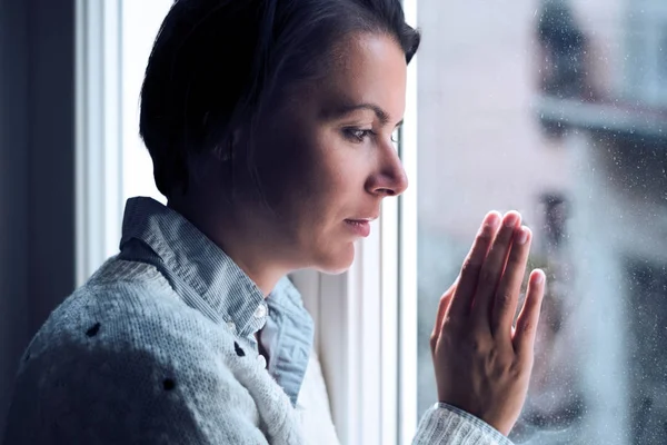 Mujer al lado de una ventana mirando hacia fuera en un estado de ánimo solitario — Foto de Stock