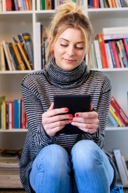 Genç kız e-kitap okuyucu renkli bookshelf yanındaki okuma