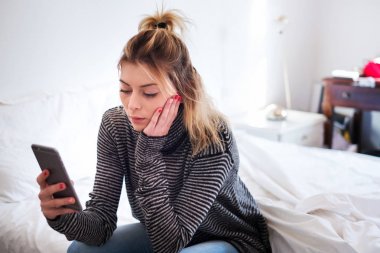 Yatağın üstüne oturan smartphone tutan kız