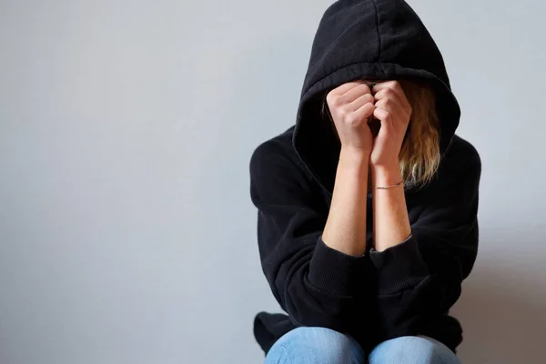 Jong meisje verbergt haar gezicht onder hooded sweatshirt geïsoleerd op b — Stockfoto