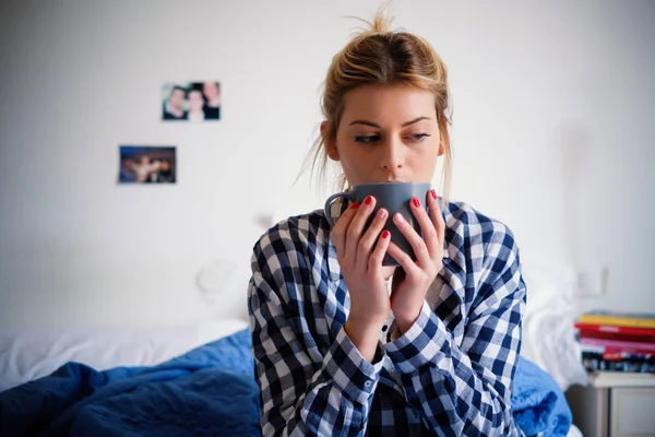 Pretty young girl drinking tea and sitting on her bed at home — Stock Photo, Image