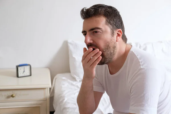 Un hombre bostezando. Él está sentado en el borde de una cama en la mañana —  Fotos de Stock