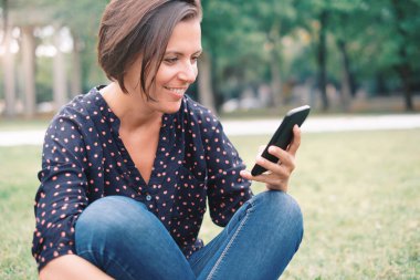 Rahat ve telefon ile çimlerde oturan kadın