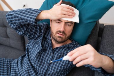 Kanepede hasta adam portresi var. Ateşi kontrol ediyor.