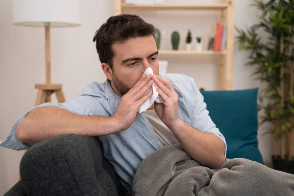 Ill man lying on the sofa blowing his nose — Stock Photo, Image