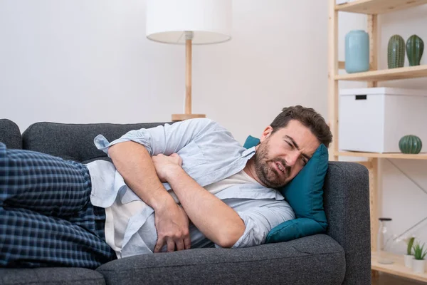 Hombre acostado en el sofá sintiendo dolor y dolor de estómago —  Fotos de Stock