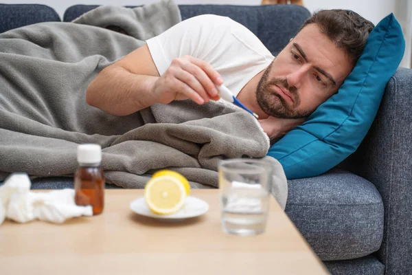 Retrato de hombre enfermo en el sofá comprobando la temperatura de la fiebre —  Fotos de Stock