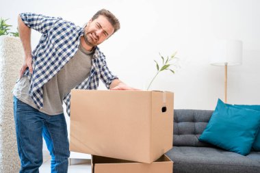 Sırtım ağrıyor. Genç adam karton kutuyu kaldırırken acı çekiyor.
