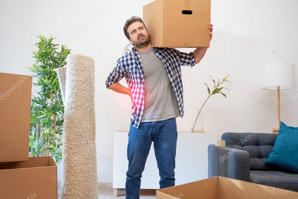 Pain in back. Young man suffering while lifting a cardboard box