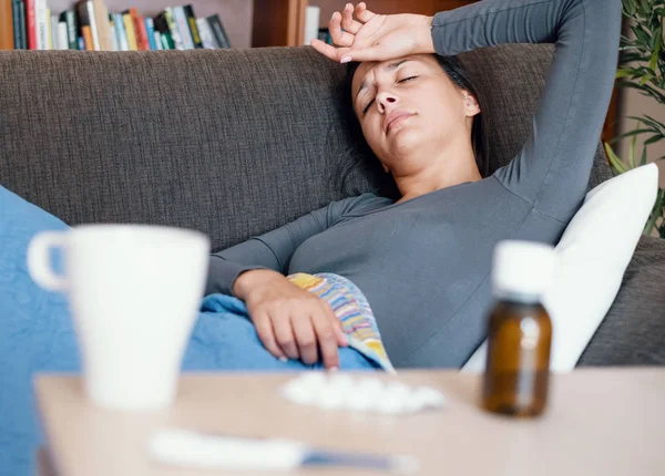 Sjuk kvinna täckt av en filt på soffan med hög feber och — Stockfoto