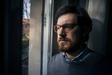 Düşünceli, endişeli adam pencereden dışarı bakıyor.