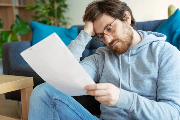 Mann liest negative Nachrichten in einem Brief zu Hause auf dem Sofa — Stockfoto
