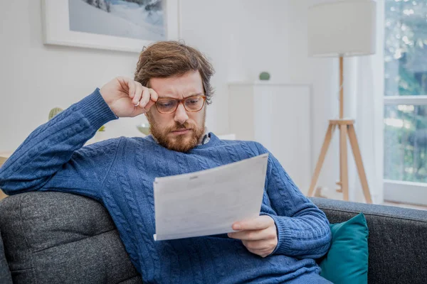 Mężczyzna czytający negatywne wiadomości w liście w domu na kanapie — Zdjęcie stockowe