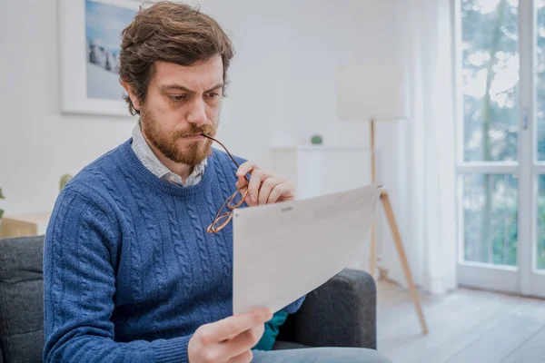 Mężczyzna czytający negatywne wiadomości w liście w domu na kanapie — Zdjęcie stockowe