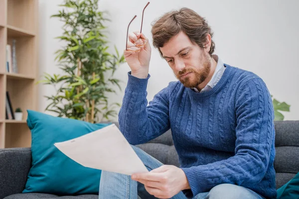 Hombre leyendo noticias negativas en una carta en casa en el sofá —  Fotos de Stock