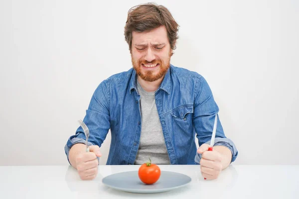 Грустный голодный человек ест овощи изолированы на белом фоне — стоковое фото