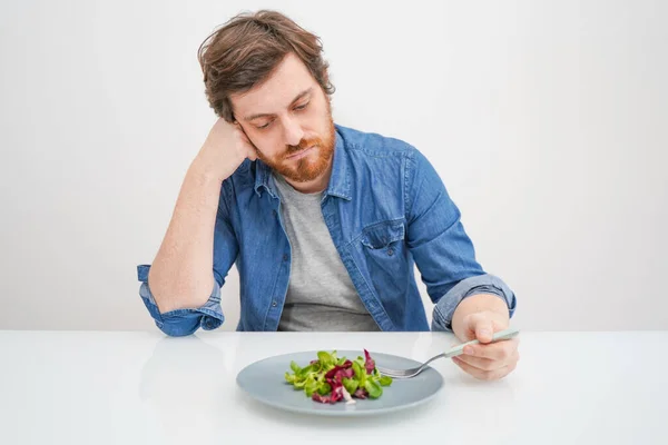 Sad hungry man eating vegetables isolated on white background — Stock Photo, Image