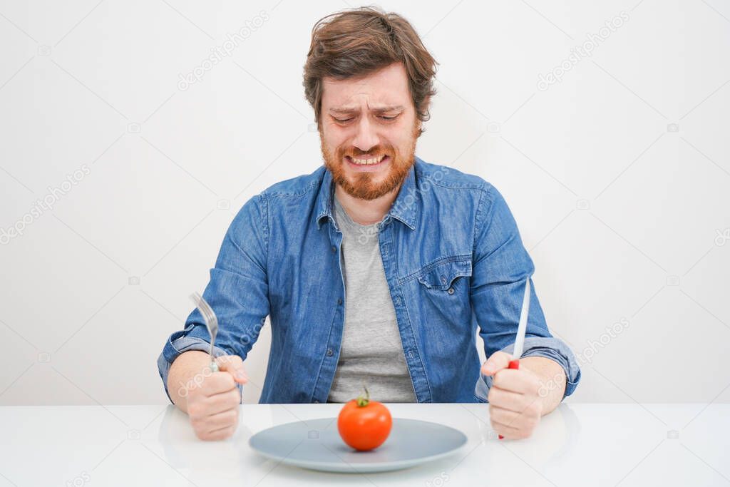 Sad hungry man eating vegetables isolated on white background