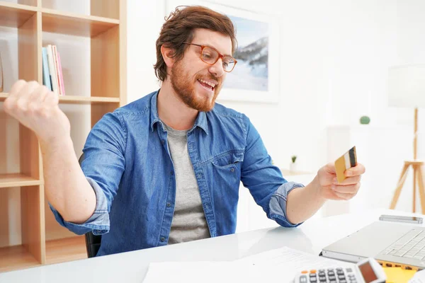 Fešák vousatý chlap držící kreditní kartu a pomocí notebooku — Stock fotografie