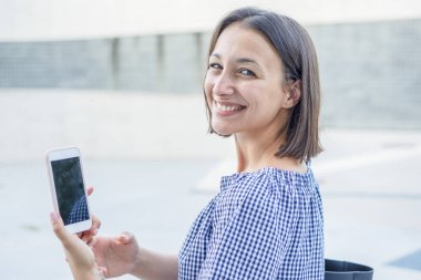 Şehir caddesinde neşeli bir kadın telefonda mesajlaşıyor.
