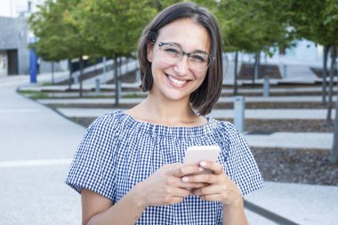 Şehir caddesinde neşeli bir kadın telefonda mesajlaşıyor.