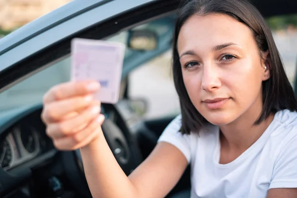 Young woman holding driver license in her car