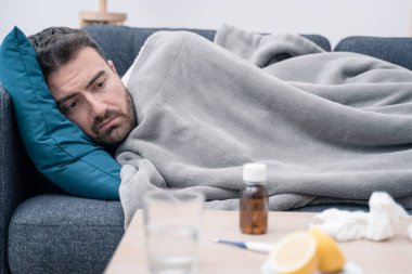 Ekoseye sarılı bir adam, evinde hasta bir şekilde yatıyor.