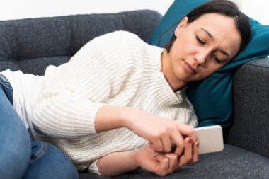 Evdeki koltukta telefonu kullanan üzgün kız.