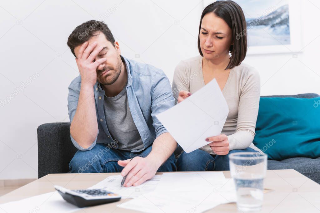 Worried couple portrait analyzing family bills at home