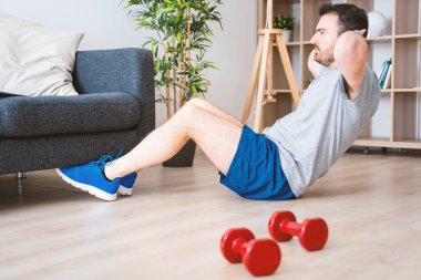 Genç adam oturma odasında karın mekiği çekiyor.