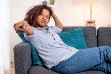 Black tired woman relaxing at home watching tv clipart