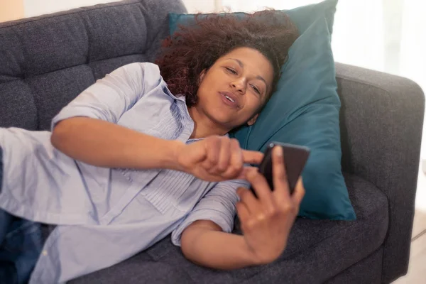 Mulher Negra Assistindo Telefone Deitado Sofá — Fotografia de Stock