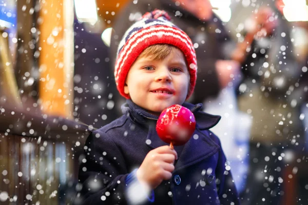 Menino pequeno comendo maçã doce no mercado de Natal — Fotografia de Stock