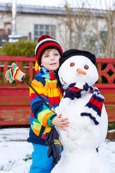 Смешной мальчик в разноцветной одежде делает снеговика — стоковое фото