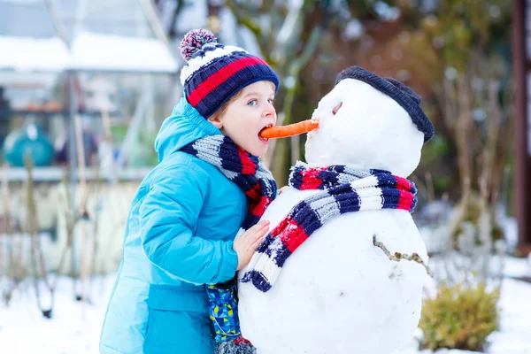 Lustige Junge in bunten Kleidern, die einen Schneemann, im Freien — Stockfoto