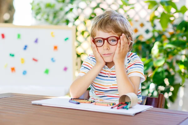 Liten skola unge pojke med glasögon håller vax kritor — Stockfoto