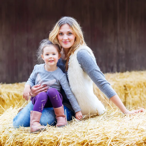 Menina feliz e mãe se divertindo com feno em uma fazenda — Fotografia de Stock