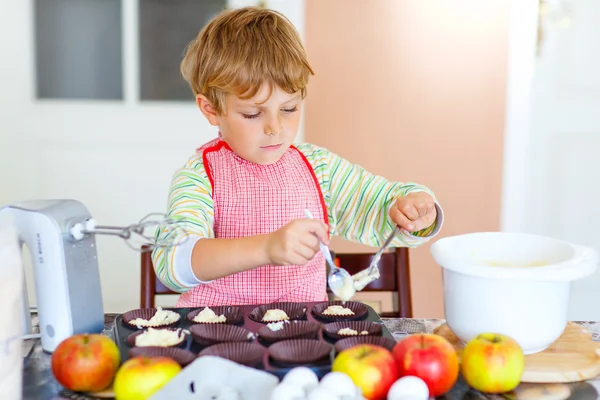 Funny blond kid boy baking apple cake indoors