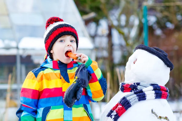 Niño gracioso en ropa colorida haciendo un muñeco de nieve, al aire libre — Foto de Stock