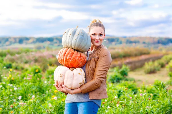 Beautiful woman with three huge pumpkins on farm — Stock Photo, Image