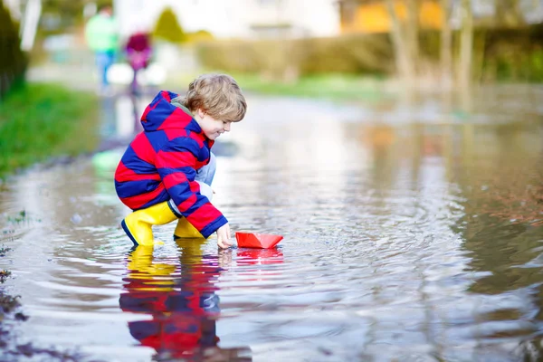 Niño jugando con papel barco por charco —  Fotos de Stock