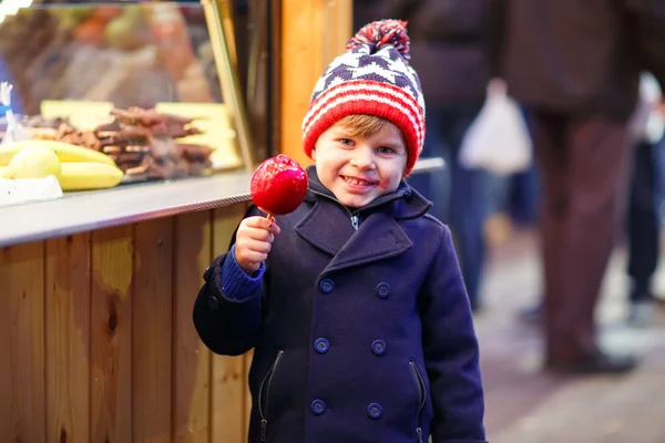 Menino pequeno comendo maçã cristalizada no mercado de Natal — Fotografia de Stock